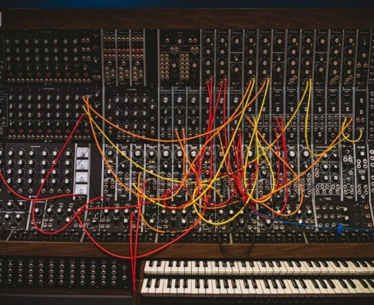 Large modular synthesizer filled with colorful patch cables and two keyboards