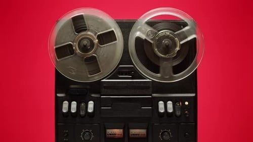Vintage reel-to-reel tape recorder with two reels against a red background